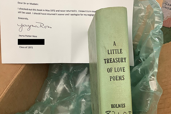 A green book titled A Little Treasury of Love Poems sits in a cardboard box with a typed letter. 